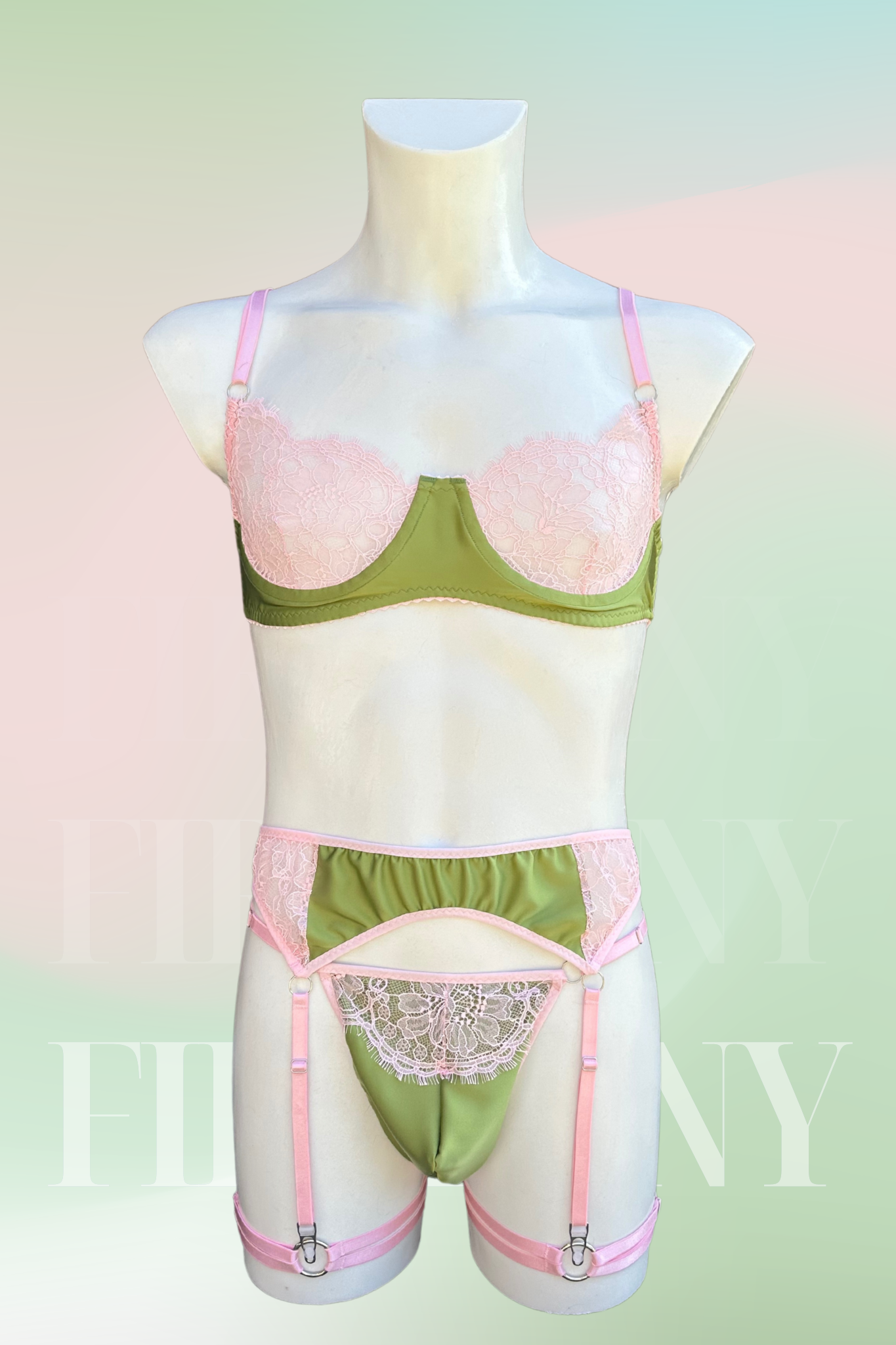 Front view of a pastel pink and olive green lace femboy lingerie set featuring a bra, thong, and garter belt on a male mannequin.