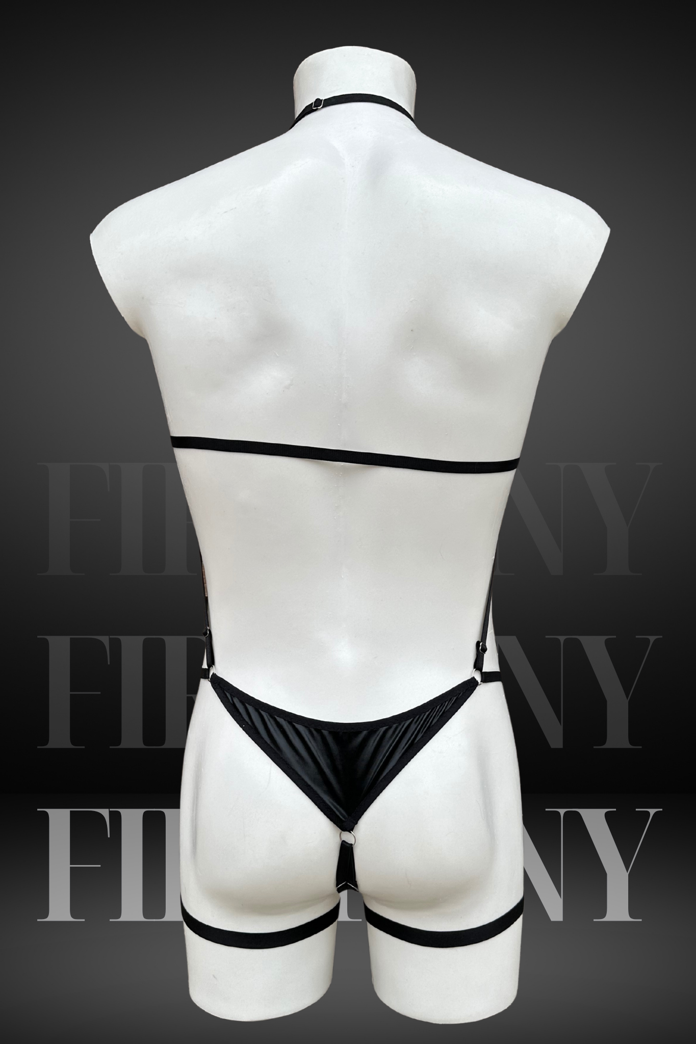 Angled back view of a black wetlook harness bodysuit for men with thong bottom and sleek fit.