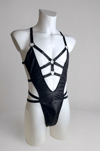 Men's vegan leather harness bodysuit, three-quarter view showing the deep V front and waist wrap straps