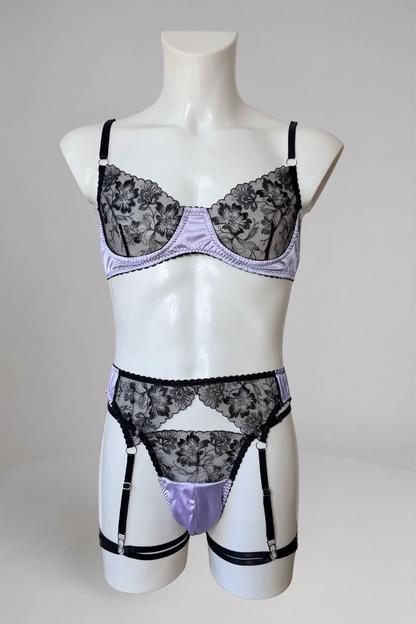Ensemble lingerie homme en satin lavande sur mannequin, vue de face : soutien-gorge en dentelle noire, string en satin et porte-jarretelles