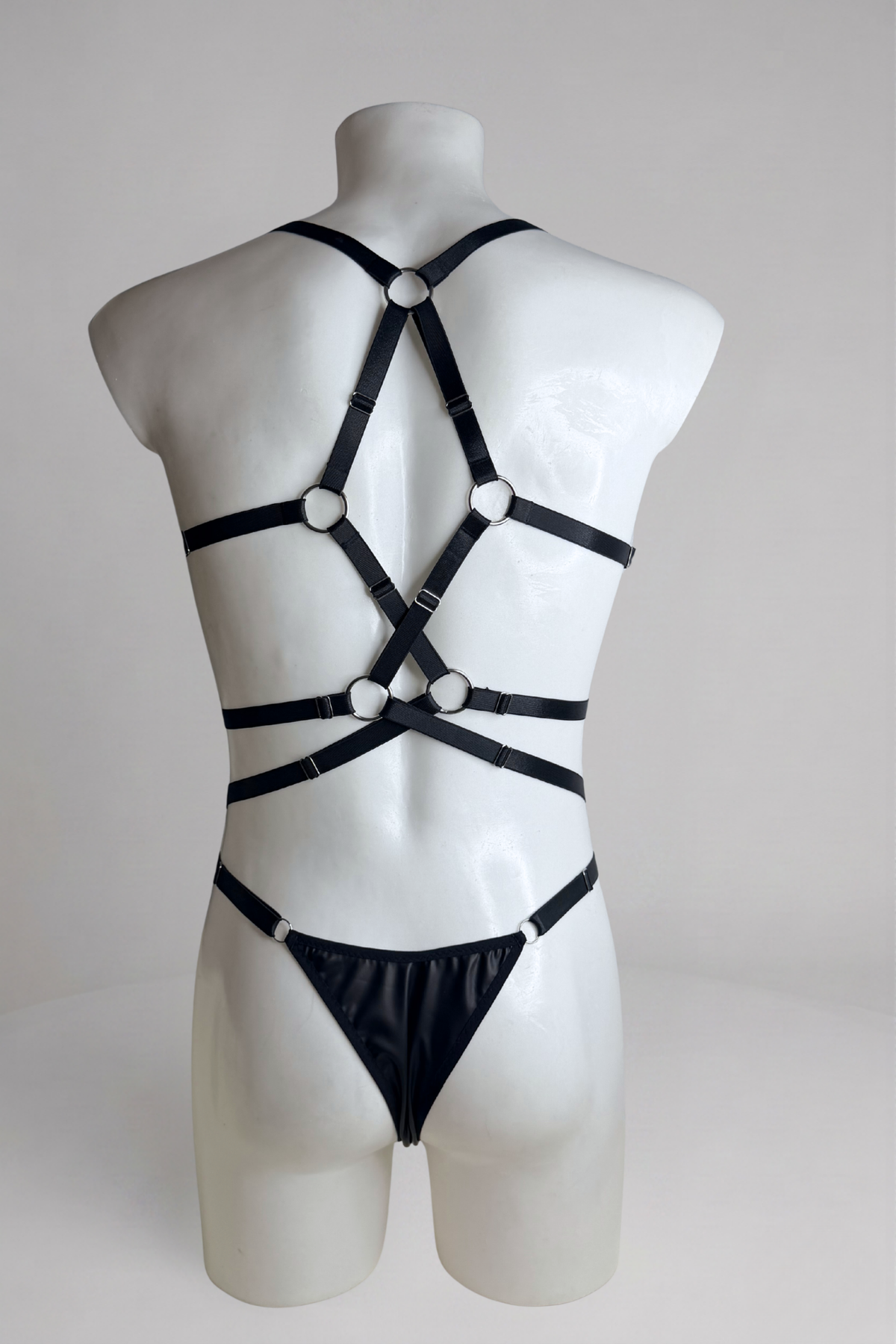 Back view of black harness bodysuit for men: crisscross elastic straps with O-rings and thong back
