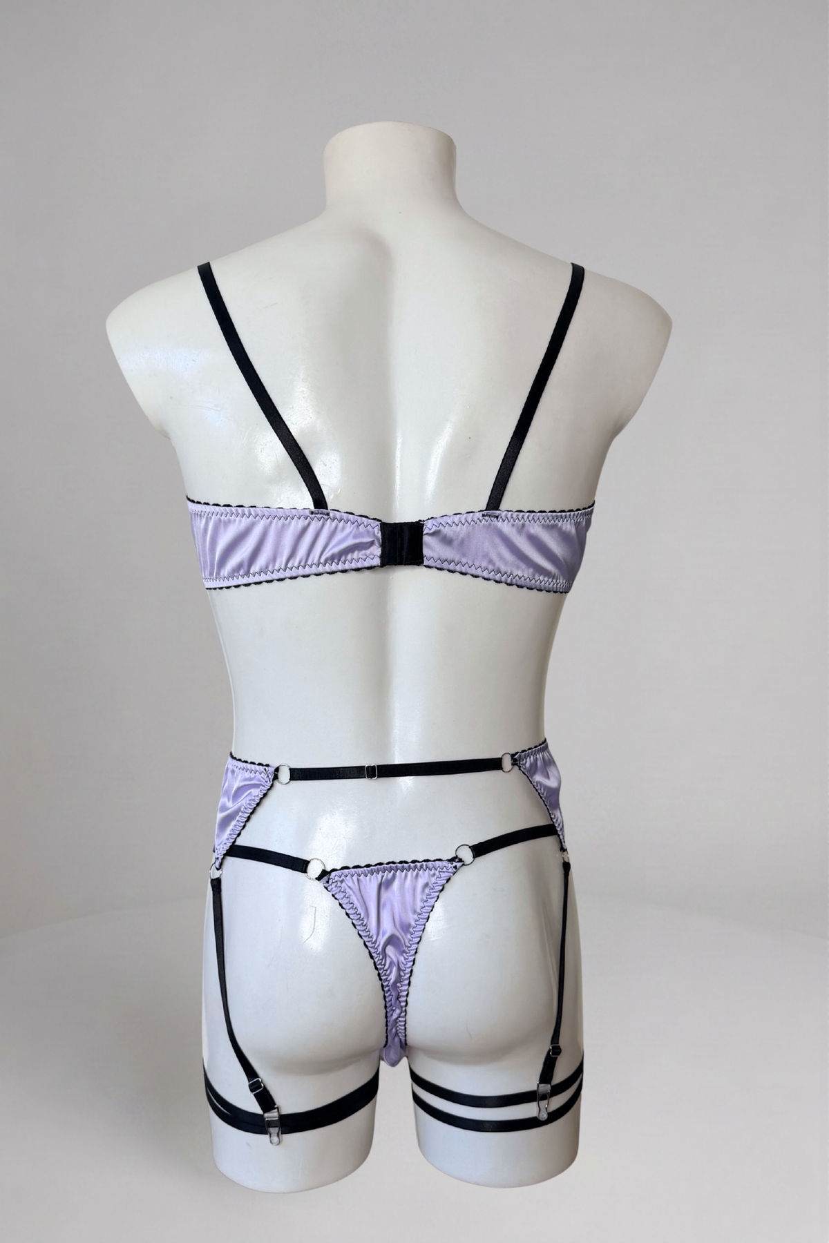 Vue de dos de l'ensemble lingerie homme en satin lavande : bande du soutien-gorge, dos string et jarretelles avec bandes de cuisse