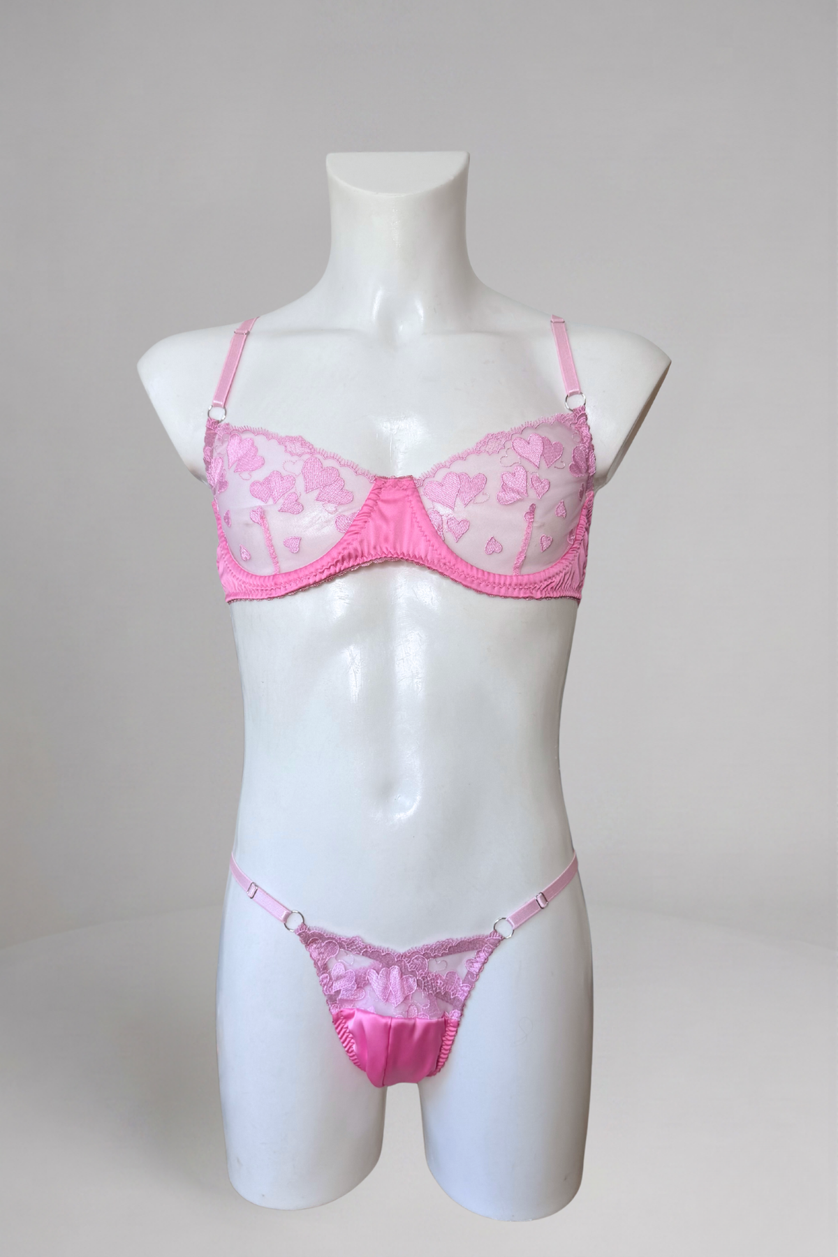 Ensemble soutien-gorge et string homme en dentelle cœur rose sur mannequin de vitrine, vue de face