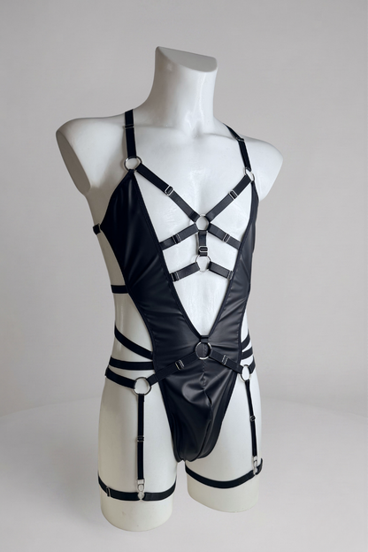 Black harness bodysuit for men with garter belt, three-quarter view: chest O-rings, waist strap and leg straps
