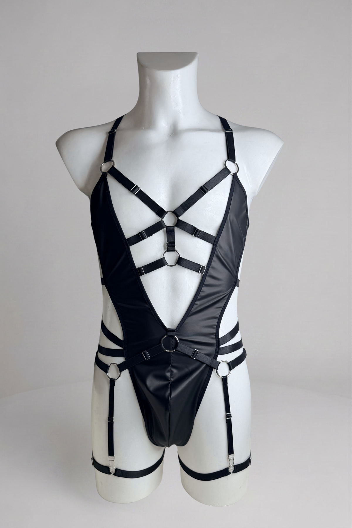 Men's vegan leather bodysuit with garter belt on mannequin, front view: deep V, O-ring waist strap and garter straps
