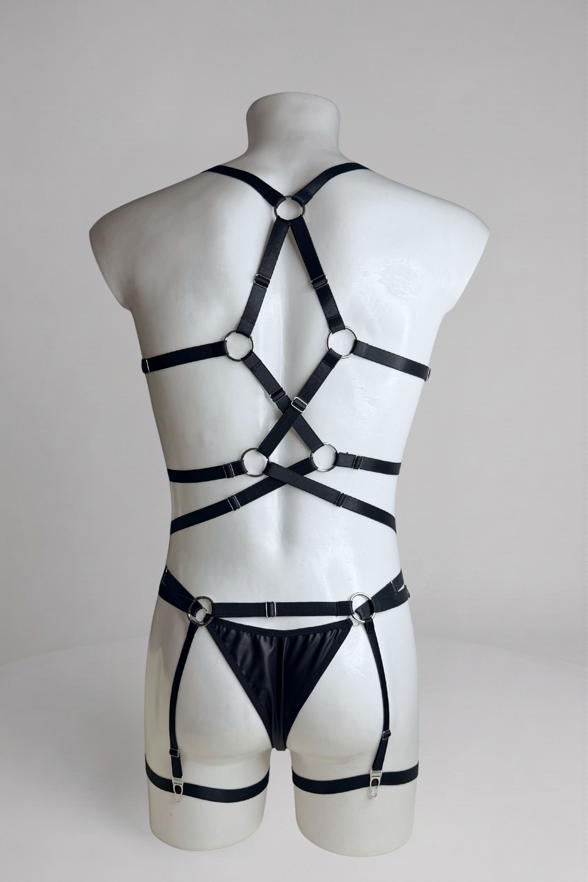 Back view of men's vegan leather bodysuit with garter belt: crisscross straps, thong back and garter straps