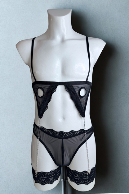 Black cage bra set for men on a mannequin, front view: mesh panels with round cut-outs, chains and lace thigh garters