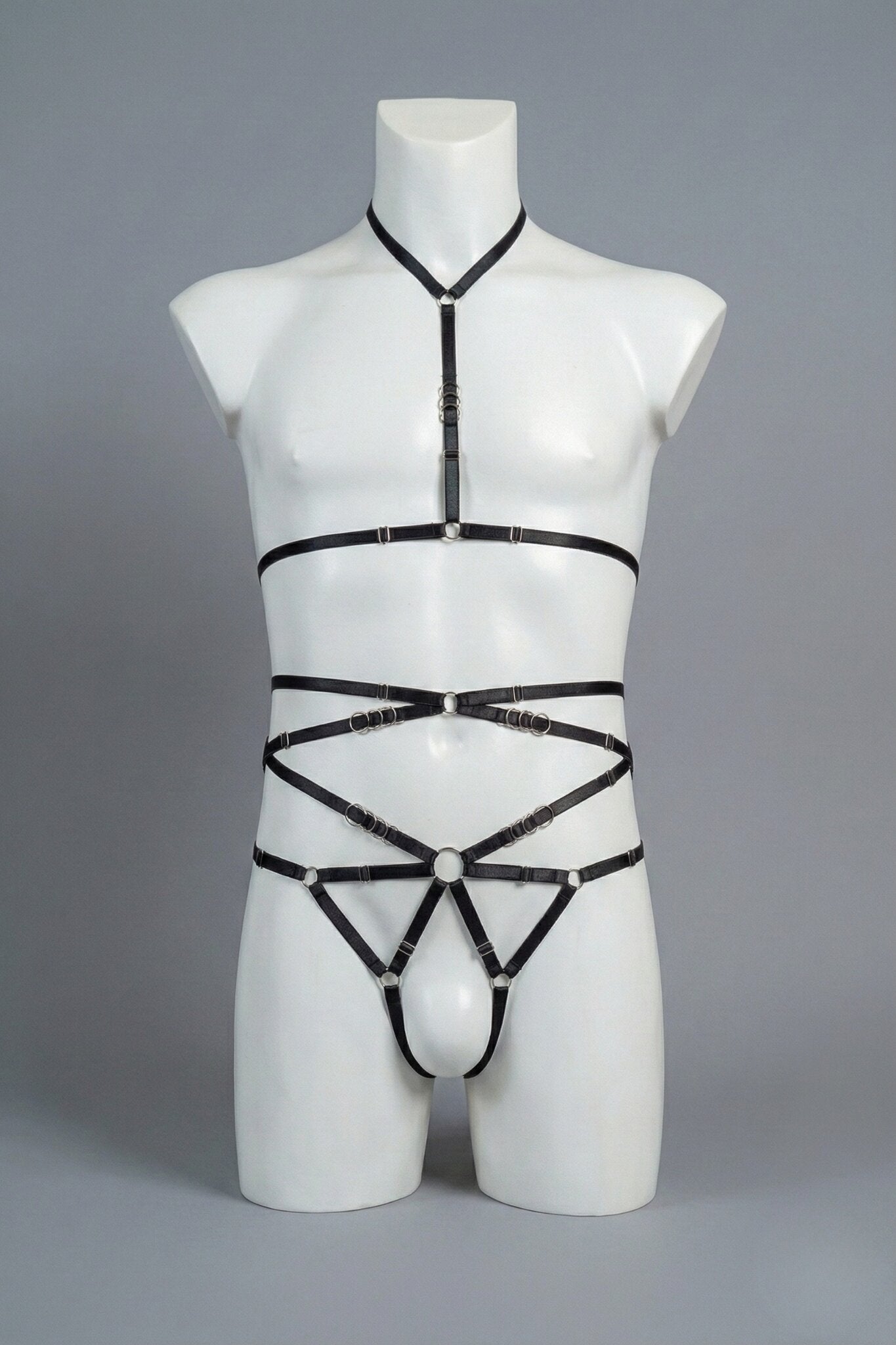 Black strappy body harness set for men on mannequin - choker harness top and open-frame harness bottom with silver o-rings, front view