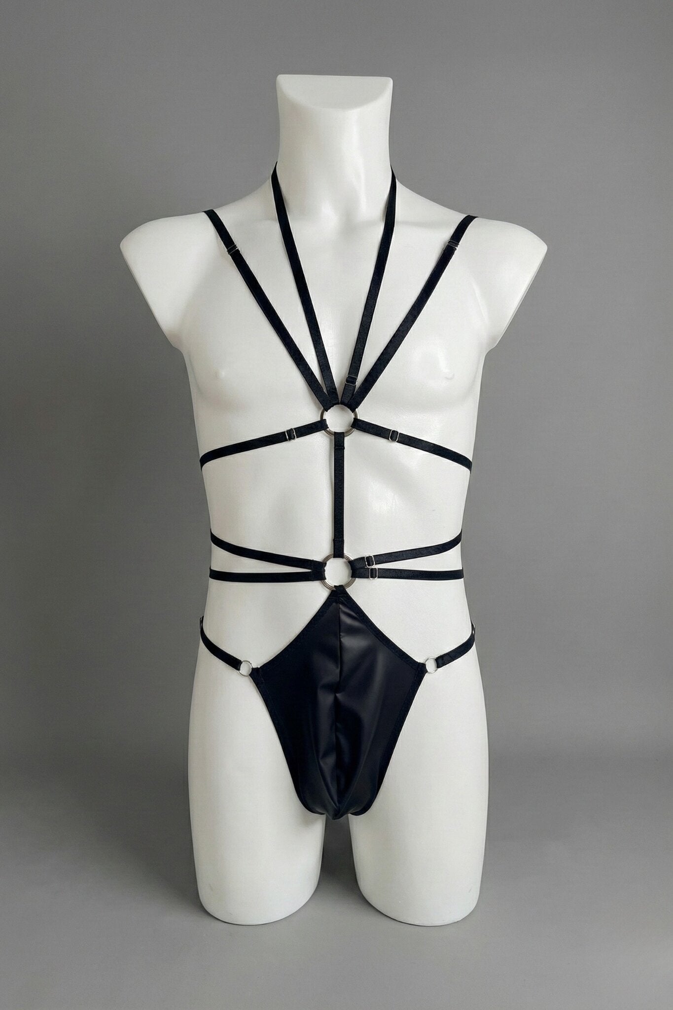 Black strappy harness bodysuit for men on mannequin - elastic straps with o-rings and faux leather thong, front view