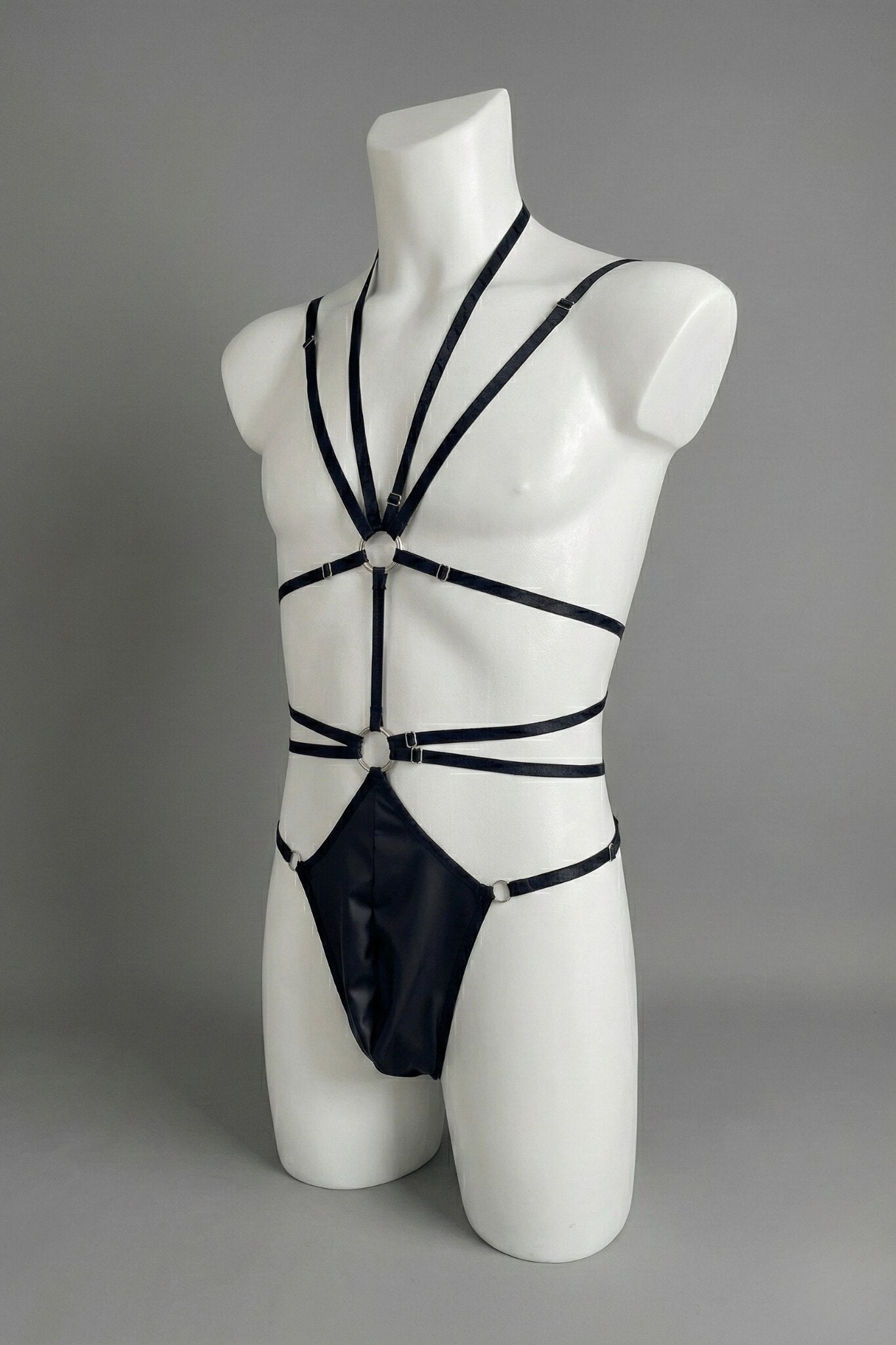 Black strappy harness bodysuit for men - three-quarter view showing chest o-ring and faux leather front